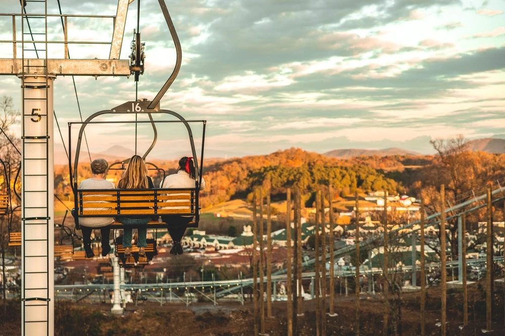 3 people riding chairlift from SkyLand Ranch facing Smoky Mountain fall scenery